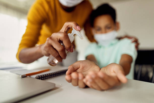 Close-up of black mother using hand sanitizer and cleaning son's hands at home during coronavirus epidemic.
